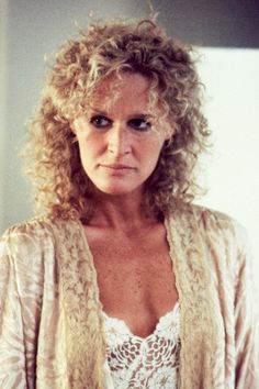 a woman with curly hair wearing a lacy top and cardigan jacket looking at the camera