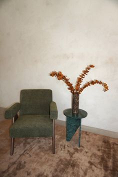 two chairs and a vase with flowers in it on a carpeted floor next to a wall