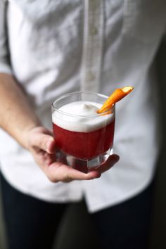 a person holding a drink with an orange garnish on the rim in their hand