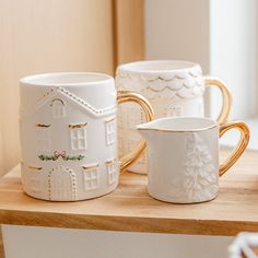 three white and gold mugs sitting on top of a wooden table