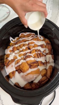 a person pouring milk over cinnamon rolls in a crock pot on a counter top