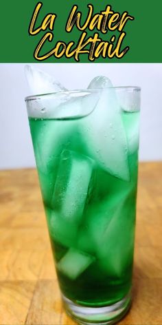 a tall glass filled with ice and green liquid on top of a wooden table next to a