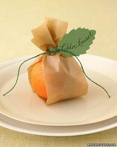 an orange sitting on top of a white plate next to a green leaf and name tag