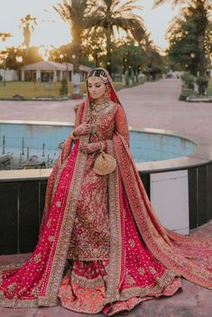 a woman in a red and gold bridal gown standing next to a swimming pool