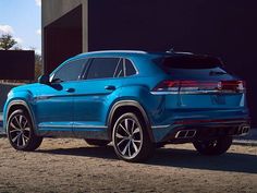 the rear end of a blue volkswagen suv parked in front of a building on a dirt road