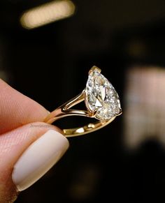 a close up of a person's hand holding a ring with a pear shaped diamond on it