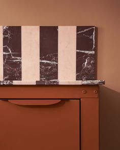 a brown cabinet with marble top and two vertical stripes on the front, against a tan wall