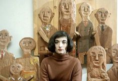 a woman sitting on a chair in front of some wooden carvings and sculptures that look like human heads