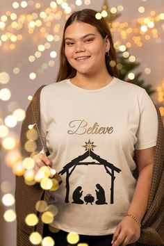 a woman wearing a t - shirt that says believe with a nativity scene on it