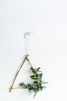 a twig hanging from the side of a white wall with greenery on it