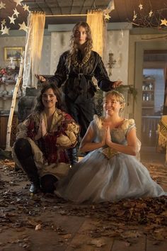 three women dressed in period costumes sitting on the floor with one woman kneeling down and another standing up