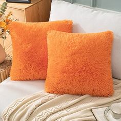 two orange pillows sitting on top of a white bed next to a vase with flowers