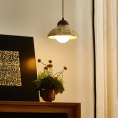 a lamp hanging over a table next to a vase with flowers in it and a painting on the wall