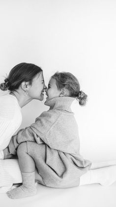 a mother kissing her daughter's cheek while sitting on the floor in black and white