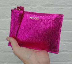 a hand holding a pink purse with the word necon on it in gold lettering