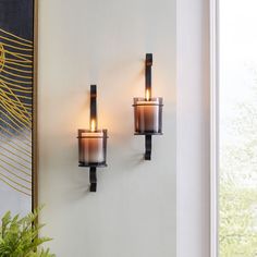 two candles are lit on the wall next to a potted plant