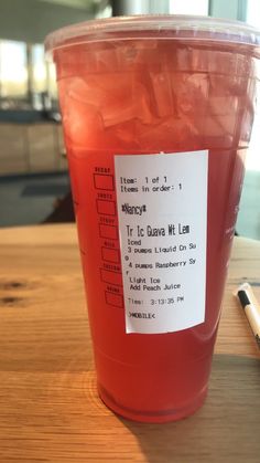 a plastic cup filled with liquid sitting on top of a wooden table next to a pen