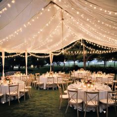 a large tent with tables and chairs set up for an outdoor wedding reception at night