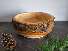 a wooden bowl sitting on top of a table next to a pine cone