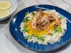 a blue plate topped with rice and shrimp next to a bowl of lemon wedges