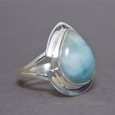 SKU: SS-058Material: 925 stamped sterling silverGemstone(s): Larimar (N)Gemstone Dimensions: 18 X 24 X 3 mmRing Size: US 9Weight: 7.0 gramsThis stunning Larimar ring features a large pear Larimar cabochon, set in a unique split bezel frame and a split shank ring. The split bezel frame adds the distinctiveness that makes this ring unique! The Larimar is a beautiful blend of ocean green and white waves. Teardrop Moonstone Ring In Sterling Silver, Sterling Silver Teardrop Opal Ring, Sterling Silver Teardrop Rings, Teardrop Opal Ring In Sterling Silver, Elegant Teardrop Opal Ring In Sterling Silver, Sterling Silver Teardrop Moonstone Ring, Sterling Silver Pear-shaped Gemstone Ring, Silver Teardrop Opal Ring In Sterling Silver, Sterling Silver Teardrop Gemstones For Anniversary