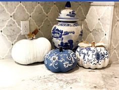 three blue and white pumpkins sitting next to each other on a counter with an ornate wallpaper