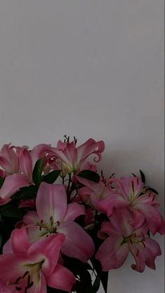 some pink flowers are in a vase on a white tablecloth and the wall is behind them