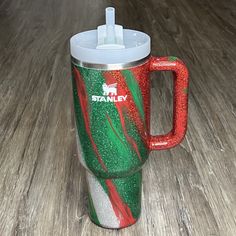 a red, green and white coffee cup sitting on top of a wooden table next to a straw