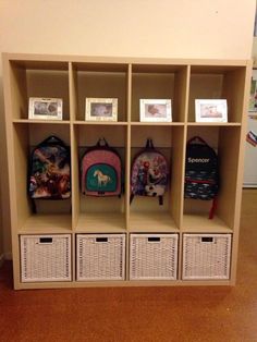 a bookcase with baskets and backpacks on it in a room next to a wall