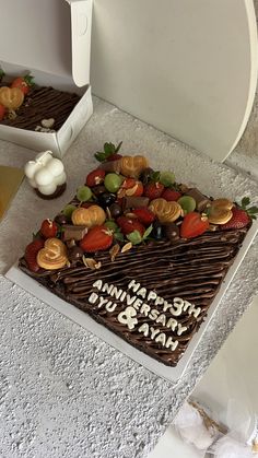 a birthday cake with strawberries and other toppings sits on a table next to an open toilet