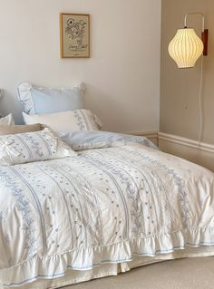 a bed with white and green comforter next to a wall light in a bedroom