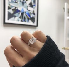 a woman's hand with a diamond ring on top of her finger in front of a painting