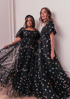 two women standing next to each other wearing black dresses with gold stars on the skirt