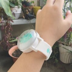 a person's wrist with a watch on it and some plants in the background