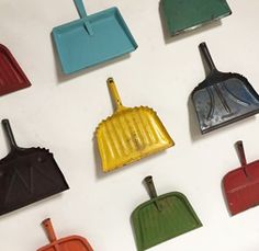 several different colored dustpans and brooms on a white surface