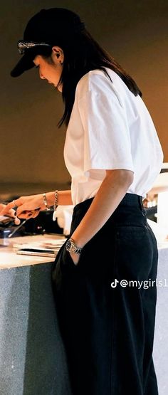 a woman standing in front of a counter using a laptop computer while wearing a hat