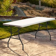 a white table sitting on top of a cement ground next to a lush green field