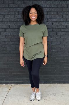 a woman standing in front of a brick wall wearing leggings and a t - shirt