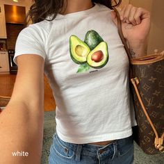 "Rock your day with this coquette-inspired avocado T-shirt! Perfect for Y2K fashion enthusiasts, this comfy cotton tee features a stunning watercolor avocado print. Whether you're going out with friends or keeping it casual at home, this shirt adds a trendy touch to any outfit! 🥑✨  Looking for a graphic baby tee nostalgic of the 90s? Bring your Y2K outfit dreams to life with our newest collection. This classic baby tee will fit like a well-loved favorite from its first wear.  ✨PLEASE NOTE: The Trendy Fitted Fruit Print Top, Fitted Short Sleeve T-shirt With Fruit Print, Y2k Cotton T-shirt With Fruit Print, Y2k Style Cotton T-shirt With Fruit Print, Fitted Short Sleeve Tops With Fruit Print, Trendy Green Tops With Fruit Print, Cute Green Top With Fruit Print, Baby Tee Aesthetic, Aesthetic Watercolor