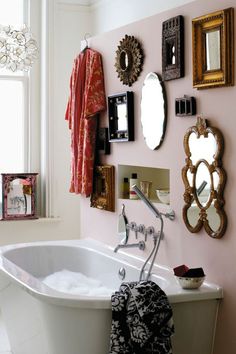 a bath tub sitting under a mirror next to a wall filled with pictures and mirrors