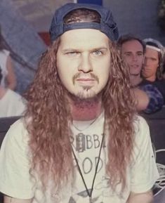 a man with long hair wearing a hat and looking at the camera while others look on