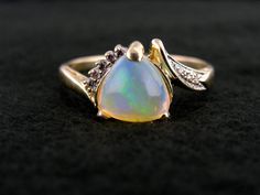 "Polished to perfection and filled with glitters of light in every shade of the rainbow, this gorgeous opal gemstone shines with fire from each of its three facets. We love the nearly heart shaped profile of this trillion cut stone, and the slightly asymetrical flow it gives the gold and diamond setting! Metal: 14K Yellow Gold Gem: Opal 1.53 Carats Gem Measurements: 8.6 mm, Trillion Cut Accents: 8 Diamonds totaling .10 Carat Ring Size: 11 Marks: \"14K\" Stamped on the inside band SKU #: VW4YPF-N Iridescent Opal Jewelry For Anniversary, Elegant Opal Heart Cut Jewelry, Opal Ring With Diamond Accents For Gift, Elegant Heart Cut Opal Jewelry, Gift Opal Ring With Diamond Accents, Dazzling Opal Gemstone Ring Gift, Elegant Iridescent Opal Ring For Anniversary, Multicolor Opal Jewelry For Anniversary, Elegant Multicolor Cabochon Opal Ring