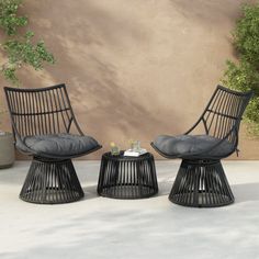 two black wicker chairs and a small table in front of a stucco wall