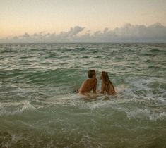 two people sitting in the ocean with their backs to each other