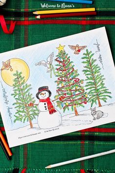 a christmas card with a snowman and trees on it, surrounded by colored pencils