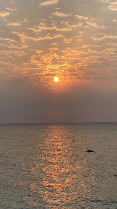 the sun is setting over the ocean with two people on surfboards in the water