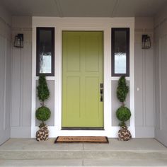 a green door with two potted plants on the front step next to an entryway