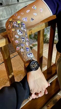 a person with tattoos on their arm holding onto a wooden bench while wearing a watch