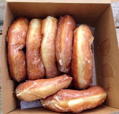 a box filled with glazed donuts sitting on top of a wooden table next to each other