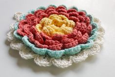 a crocheted flower is sitting on a table top with white and red yarn